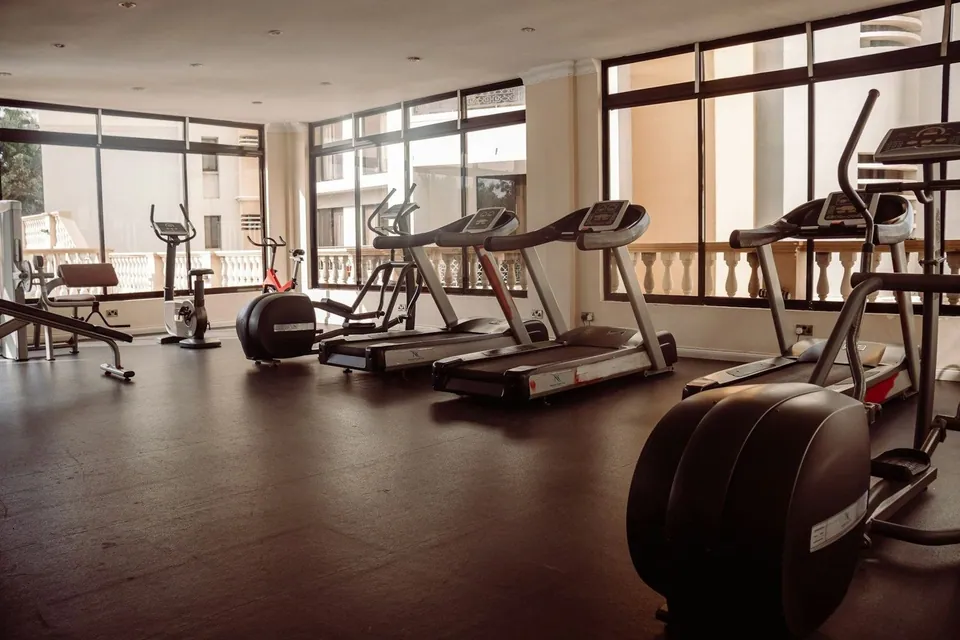 Treadmills and cross trainers beside bright gym windows
