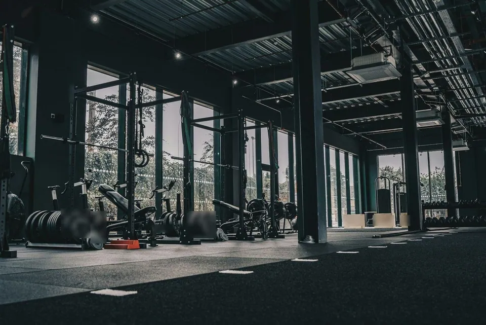 Row of power racks with barbells beside tall gym windows