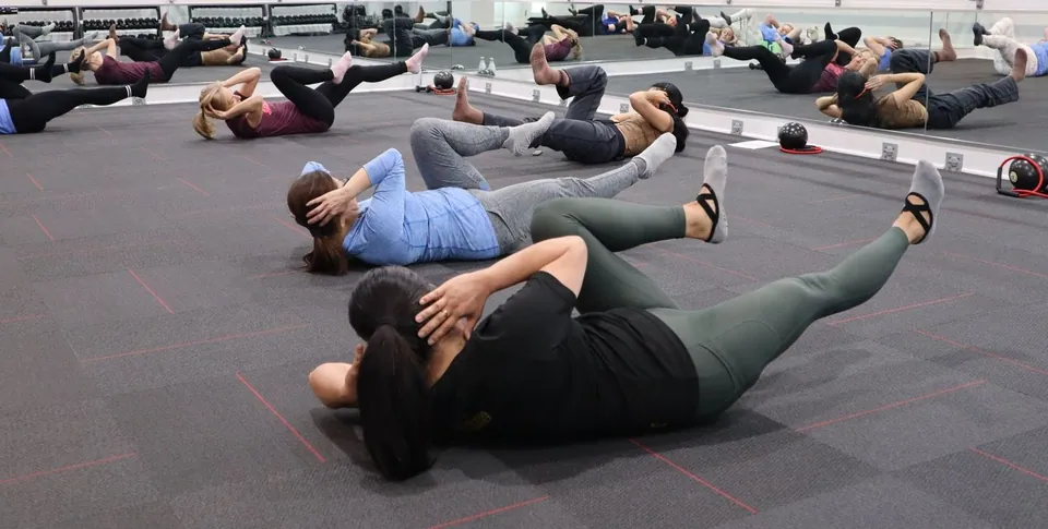 Group fitness class doing core exercises on a bright studio floor