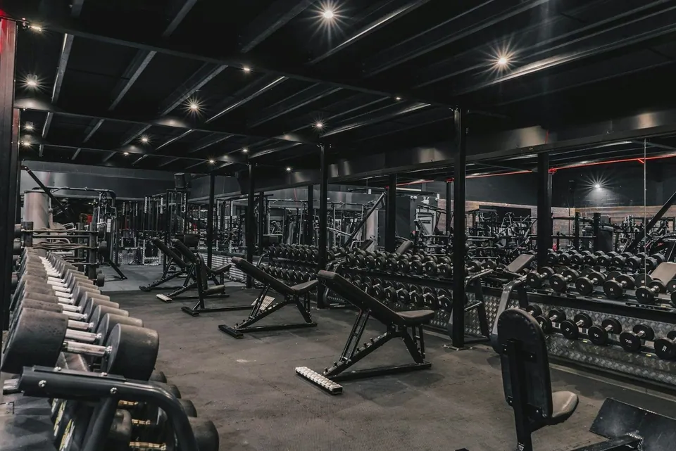 Dark moody gym floor with dumbbell racks and benches
